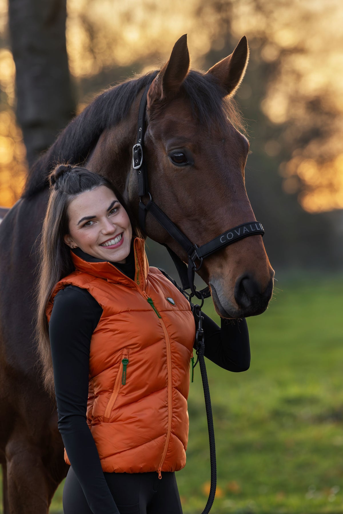 Cavalière en doudoune sans manches orange, la tête de son cheval contre elle