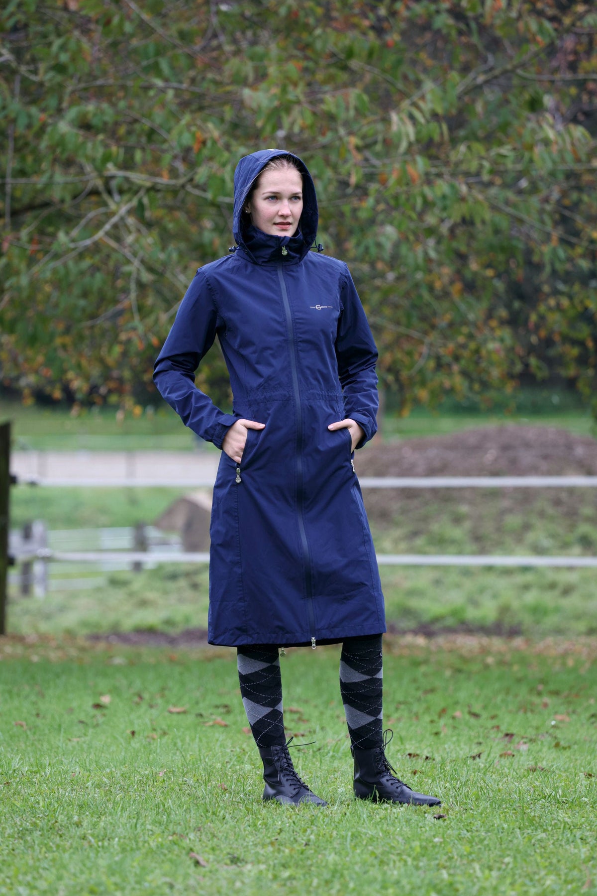 Cavalière en manteau de pluie long bleu marine, debout au pré