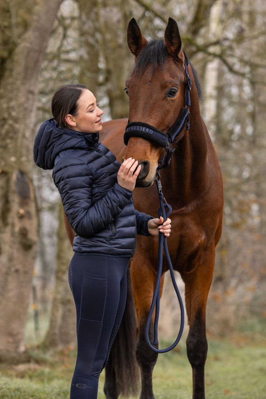 Cavalière en veste matelassée avec son cheval au pré