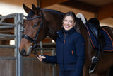 Cavalière en blouson bleu marine tenant son cheval à l'écurie