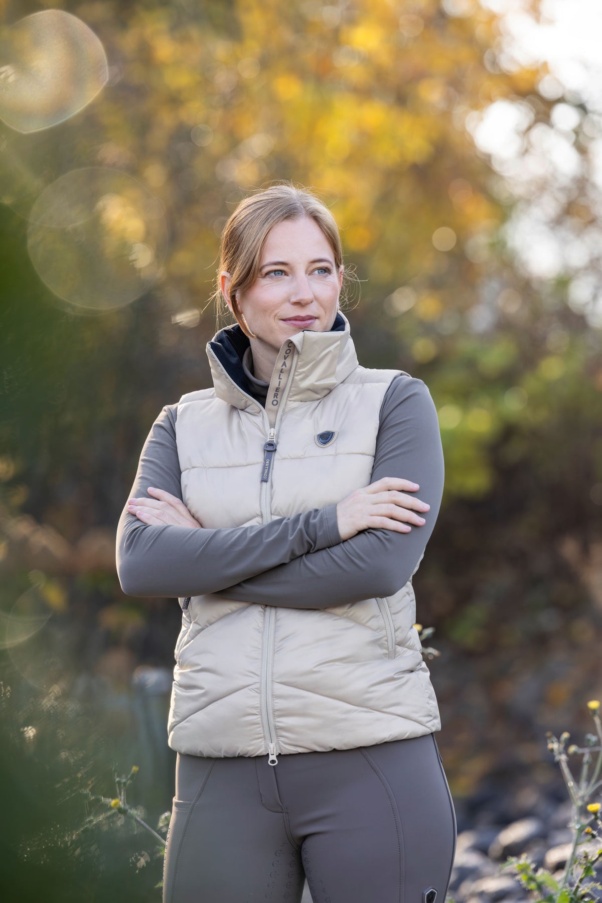 Cavalière en doudoune beige, bras croisés, dehors à l'automne
