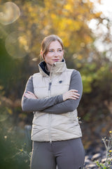 Cavalière en doudoune beige, bras croisés, dehors à l'automne