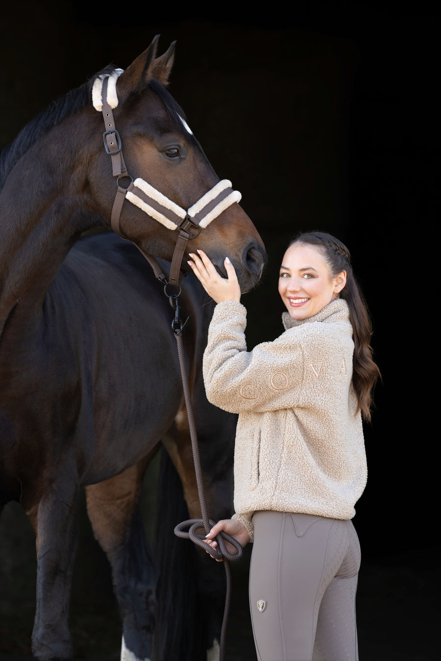 Cavalière en sweat Teddy beige caressant la tête de son cheval